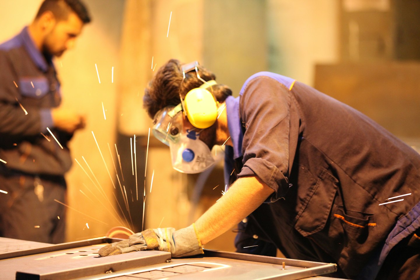 Mann schleift Metall in einer Werkstatt, Funken fliegen.